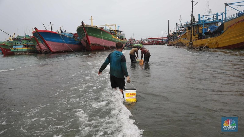 Anak Buah Kapal (ABK) melintasi banjir rob saat cuaca buruk di Pelabuhan Muara Baru, Penjaringan, Jakarta Utara, Rabu (28/12/2022). Badan Meteorologi Klimatologi dan Geofisika (BMKG) menyampaikan ada potensi cuaca ekstrem terjadi di sejumlah wilayah di Indonesia. (վ/ Muhammad Sabki)