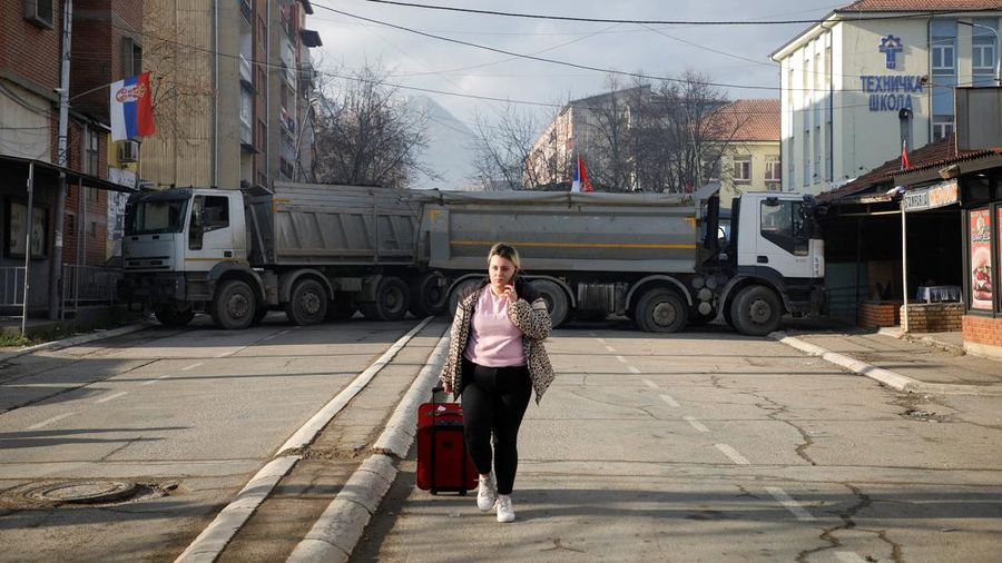 Seorang wanita berjalan di dekat penghalang jalan, di bagian utara kota Mitrovica, Kosovo, Selasa (27/12/2022).  Sejak November, Kosovo bergejolak usai ratusan pekerja etnis Serbia ramai-ramai mengundurkan diri. Mereka memprotes keputusan kontroversial pemerintah Kosovo yang melarang orang Serbia di negara itu menggunakan plat nomor dari Beograd. (REUTERS/Florion Goga)