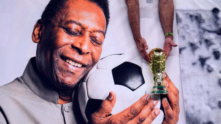Seorang penggemar Brasil memegang replika trofi Piala Dunia di atas foto mantan pemain Pele jelang pertandingan Grup G Piala Dunia FIFA di Stadion Lusail di Lusail, Qatar. (PA Images via Getty Images)