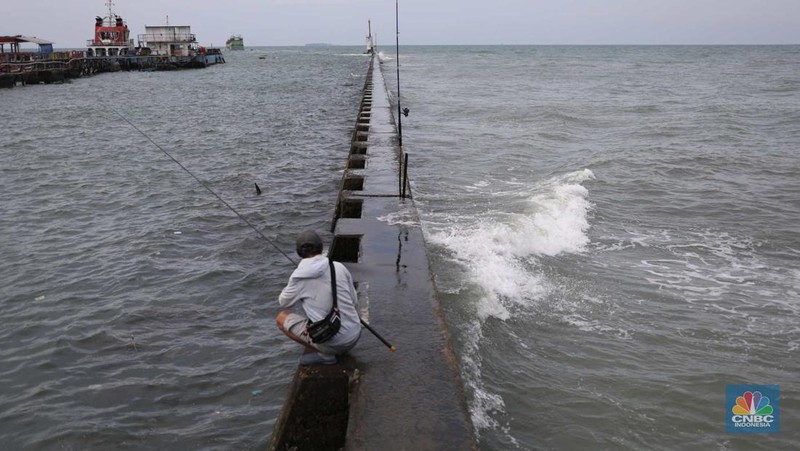 Warga memancing saat ombak besar di kawasan pelabuhan Muara Baru, Jakarta, Senin (2/1/2023). Pemerintah pusat bersama Pemerintah Provinsi DKI Jakarta tengah melakukan pembangunan tanggul pantai di wilayah utara Jakarta. (CNBC Indonesia / Tri Susilo)