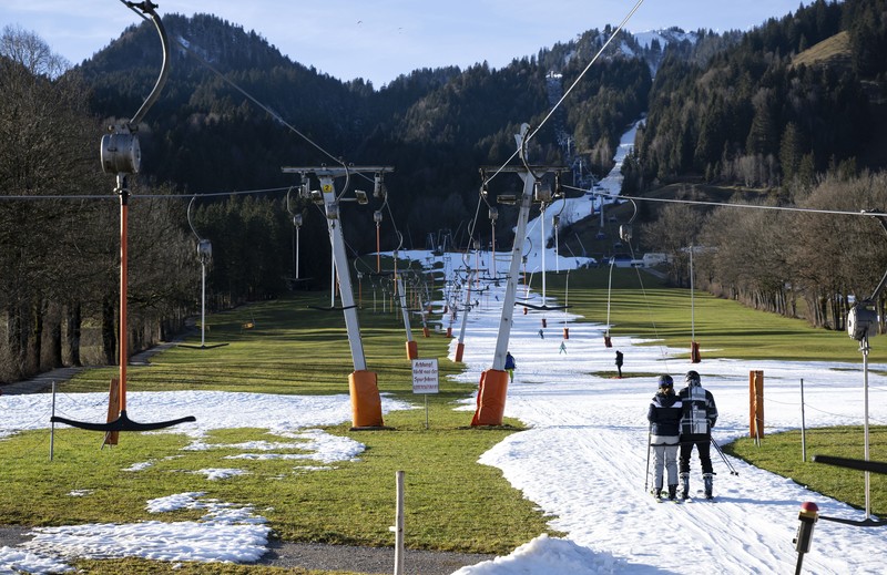 Skiers speed down a ski slope with artificial snow in the middle of a snowless field, at 1600 meters above sea level, in the alpine resort of Villars-sur-Ollon, Switzerland, Saturday, Dec. 31, 2022. Sparse snowfall and unseasonably warm weather in much of Europe is allowing green grass to blanket many mountaintops across the region where snow might normally be. It has caused headaches for ski slope operators and aficionados of Alpine white this time of year. (Laurent Gillieron/Keystone via AP)