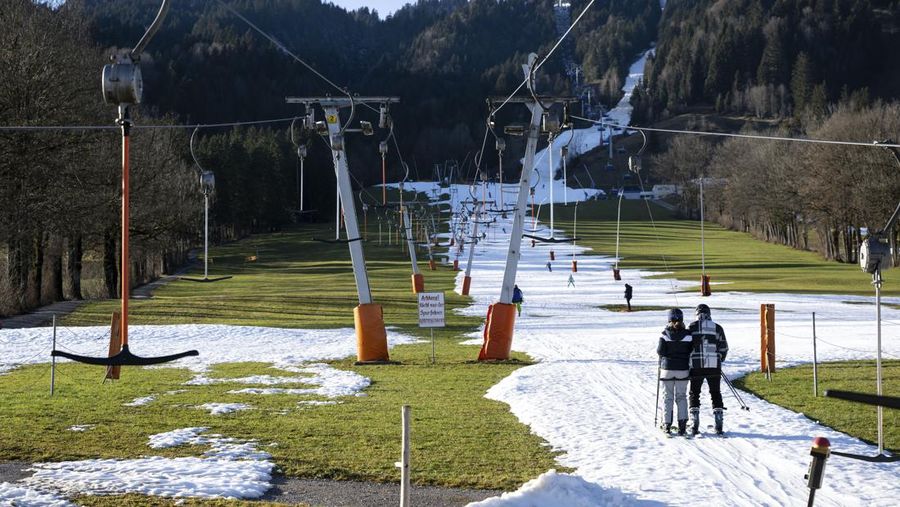 Skiers speed down a ski slope with artificial snow in the middle of a snowless field, at 1600 meters above sea level, in the alpine resort of Villars-sur-Ollon, Switzerland, Saturday, Dec. 31, 2022. Sparse snowfall and unseasonably warm weather in much of Europe is allowing green grass to blanket many mountaintops across the region where snow might normally be. It has caused headaches for ski slope operators and aficionados of Alpine white this time of year. (Laurent Gillieron/Keystone via AP)