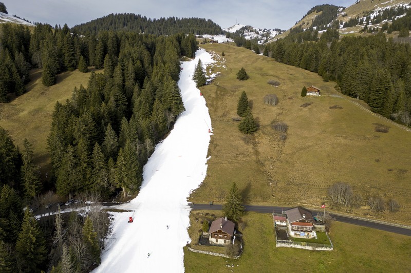 Skiers speed down a ski slope with artificial snow in the middle of a snowless field, at 1600 meters above sea level, in the alpine resort of Villars-sur-Ollon, Switzerland, Saturday, Dec. 31, 2022. Sparse snowfall and unseasonably warm weather in much of Europe is allowing green grass to blanket many mountaintops across the region where snow might normally be. It has caused headaches for ski slope operators and aficionados of Alpine white this time of year. (Laurent Gillieron/Keystone via AP)