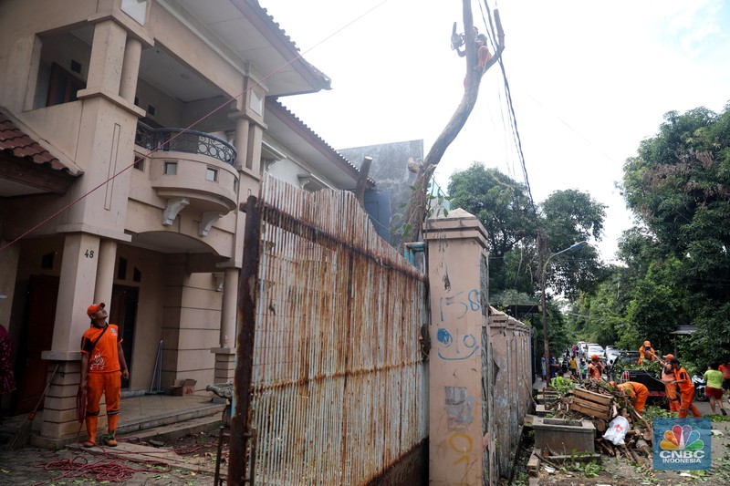 Petugas PPSU menebang pohon di depan rumah mewah terbengkalai yang viral di media sosial di Kawasan Jatinegara, Cakung, Jakarta, Kamis, (5/1/2023). (CNBC Indonesia/ Muhammad Sabki)
