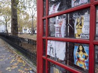 Public telephone box which has faded sex cards tacked up inside in the exclusive area of Mayfair on 2nd December 2022 in London, United Kingdom. These advertising cards for prostitutes are how people advertise for sexual services under the guise of o