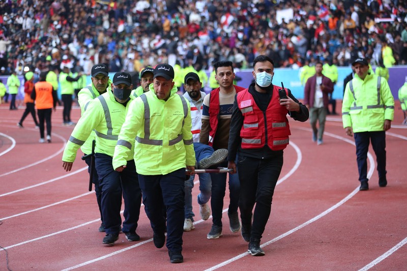Anggota tim keamanan stadion Irak membawa seorang penggemar sepak bola yang terluka ke area darurat di Stadion Internasional Basra menyusul penyerbuan menjelang pertandingan final Piala Teluk Arab malam ini antara Irak dan Oman, pada 19 Januari 2023 di Basra. - Satu orang tewas dan puluhan lainnya terluka ketika terjadi penyerbuan di luar stadion sepak bola di Irak selatan beberapa jam sebelum final Piala Teluk, kata sumber medis dan keamanan. (HUSSEIN FALEH/AFP via Getty Images)
