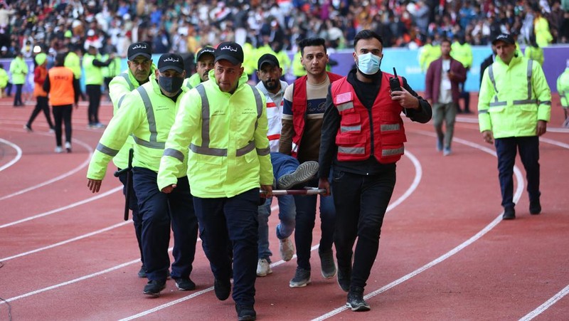 Anggota tim keamanan stadion Irak membawa seorang penggemar sepak bola yang terluka ke area darurat di Stadion Internasional Basra menyusul penyerbuan menjelang pertandingan final Piala Teluk Arab malam ini antara Irak dan Oman, pada 19 Januari 2023 di Basra. - Satu orang tewas dan puluhan lainnya terluka ketika terjadi penyerbuan di luar stadion sepak bola di Irak selatan beberapa jam sebelum final Piala Teluk, kata sumber medis dan keamanan. (HUSSEIN FALEH/AFP via Getty Images)