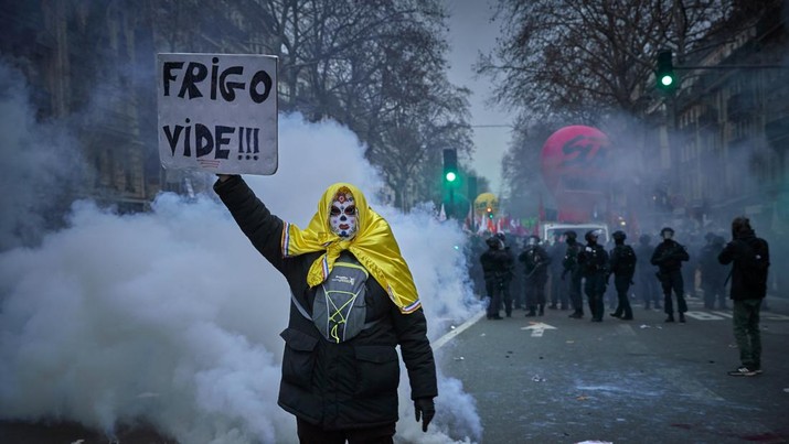 Seorang pengunjuk rasa berdiri di atas awan gas air mata memegang plakat bertuliskan 