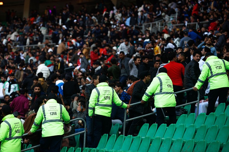 Anggota tim keamanan stadion Irak membawa seorang penggemar sepak bola yang terluka ke area darurat di Stadion Internasional Basra menyusul penyerbuan menjelang pertandingan final Piala Teluk Arab malam ini antara Irak dan Oman, pada 19 Januari 2023 di Basra. - Satu orang tewas dan puluhan lainnya terluka ketika terjadi penyerbuan di luar stadion sepak bola di Irak selatan beberapa jam sebelum final Piala Teluk, kata sumber medis dan keamanan. (HUSSEIN FALEH/AFP via Getty Images)