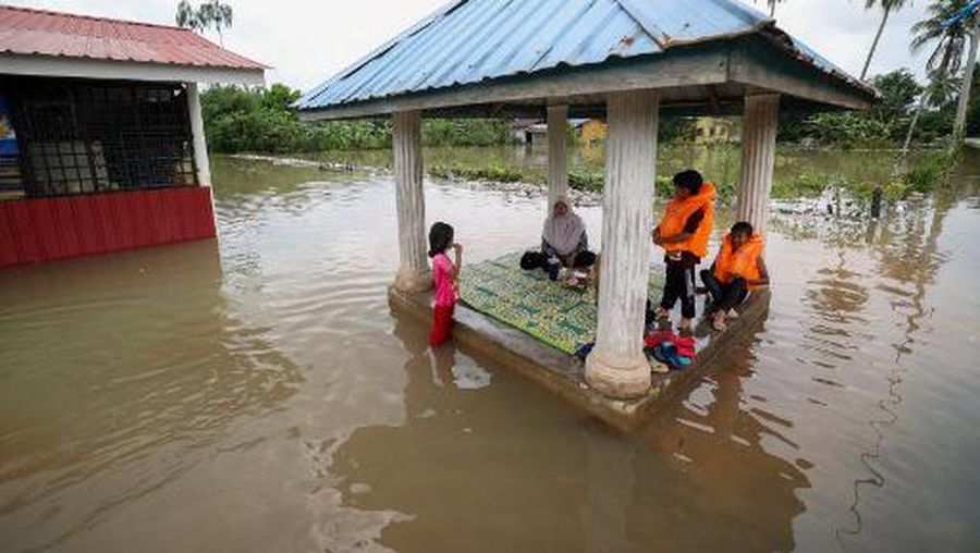 A family sits in a pergola surrounded by floodwaters in Pasir Mas in Malaysias northern Kelantan state on December 21, 2022. - At least five people were killed and over 70,000 rushed to evacuation centres in Malaysia after monsoon-triggered floods inundated large swathes of the country, authorities said December 21. (Photo by AFP) / Malaysia OUT
