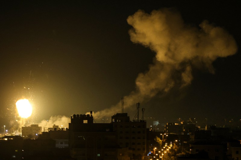 Api dan asap mengepul di atas gedung-gedung di Kota Gaza saat Israel melancarkan serangan udara ke kantong Palestina pada awal 27 Januari 2023. (AFP via Getty Images/MAHMUD HAMS) Api dan asap mengepul di atas gedung-gedung di Kota Gaza saat Israel melancarkan serangan udara ke kantong Palestina pada awal 27 Januari 2023. (AFP via Getty Images/MAHMUD HAMS)