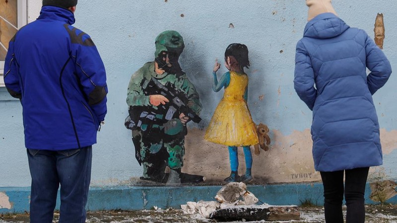 Orang-orang melihat karya seni seniman jalanan terkenal Tvboy, yang dibuat di dinding Rumah Kebudayaan, yang rusak berat selama serangan Rusia di Ukraina, di kota Irpin, di luar Kyiv, Ukraina 29 Januari 2023. (REUTERS/Valentyn Ogirenko)