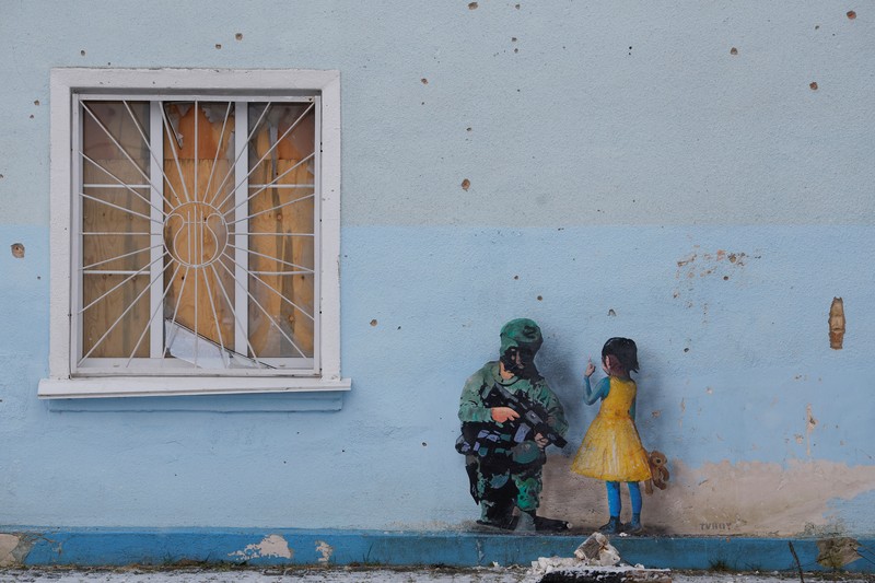 Orang-orang melihat karya seni seniman jalanan terkenal Tvboy, yang dibuat di dinding Rumah Kebudayaan, yang rusak berat selama serangan Rusia di Ukraina, di kota Irpin, di luar Kyiv, Ukraina 29 Januari 2023. (REUTERS/Valentyn Ogirenko)