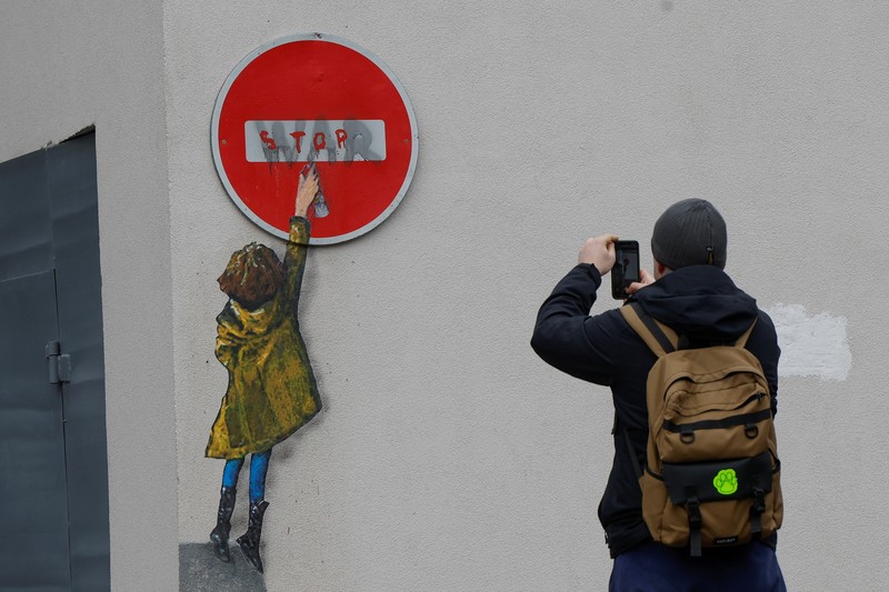 Orang-orang melihat karya seni seniman jalanan terkenal Tvboy, yang dibuat di dinding Rumah Kebudayaan, yang rusak berat selama serangan Rusia di Ukraina, di kota Irpin, di luar Kyiv, Ukraina 29 Januari 2023. (REUTERS/Valentyn Ogirenko)