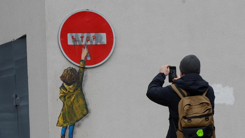 Orang-orang melihat karya seni seniman jalanan terkenal Tvboy, yang dibuat di dinding Rumah Kebudayaan, yang rusak berat selama serangan Rusia di Ukraina, di kota Irpin, di luar Kyiv, Ukraina 29 Januari 2023. (REUTERS/Valentyn Ogirenko)