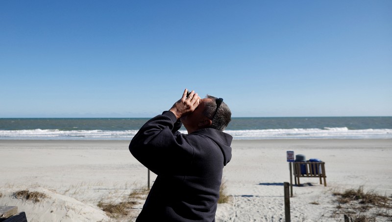Seorang pria meneropong balon mata-mata Cina yang diduga mengapung di lepas pantai di Surfside Beach, South Carolina, AS 4 Februari 2023. (REUTERS/RANDALL HILL)