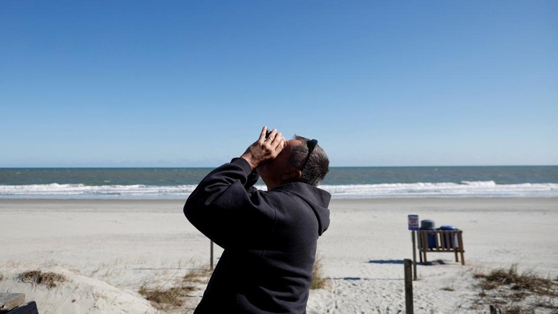 Seorang pria meneropong balon mata-mata Cina yang diduga mengapung di lepas pantai di Surfside Beach, South Carolina, AS 4 Februari 2023. (REUTERS/RANDALL HILL)