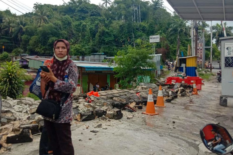 Orang-orang berdiri di atap toko yang runtuh di pelabuhan setelah gempa berkekuatan 5,1 di Jayapura, provinsi timur Indonesia Papua pada 9 Februari 2023. (FAISAL NARWAWAN/AFP via Getty Images)