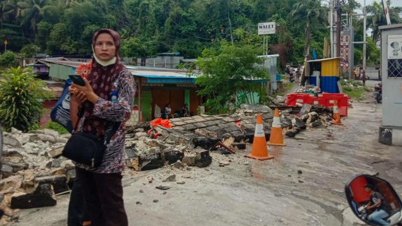 Orang-orang berdiri di atap toko yang runtuh di pelabuhan setelah gempa berkekuatan 5,1 di Jayapura, provinsi timur Indonesia Papua pada 9 Februari 2023. (FAISAL NARWAWAN/AFP via Getty Images)