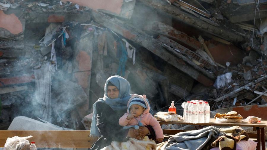 A woman holding a child sits by a collapsed building as search for survivors continues, in the aftermath of a deadly earthquake in Hatay, Turkey, February 10, 2023. REUTERS/Umit Bektas

 TPX IMAGES OF THE DAY
