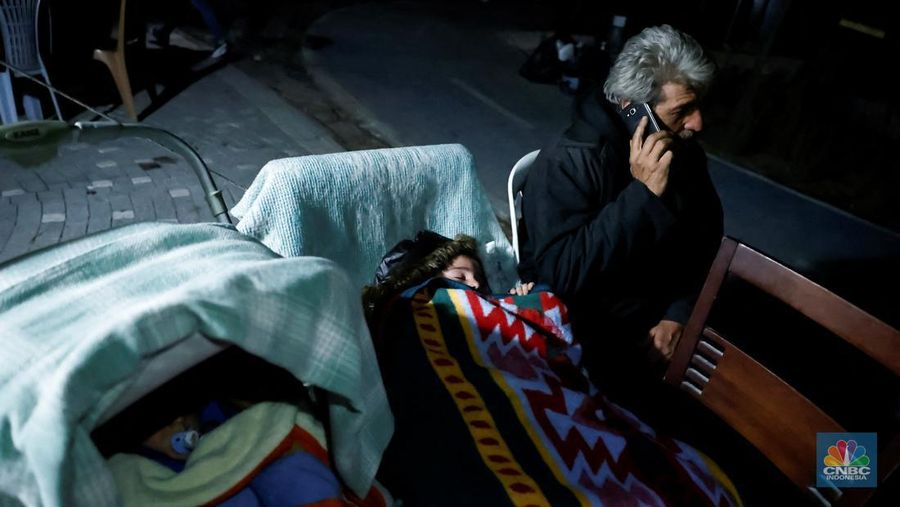 Seorang pria menggunakan smartphone di samping anak-anak yang sedang tidur di luar setelah gempa bumi di Antakya di provinsi Hatay, Turki, 20 Februari 2023. (REUTERS/Clodagh Kilcoyne)