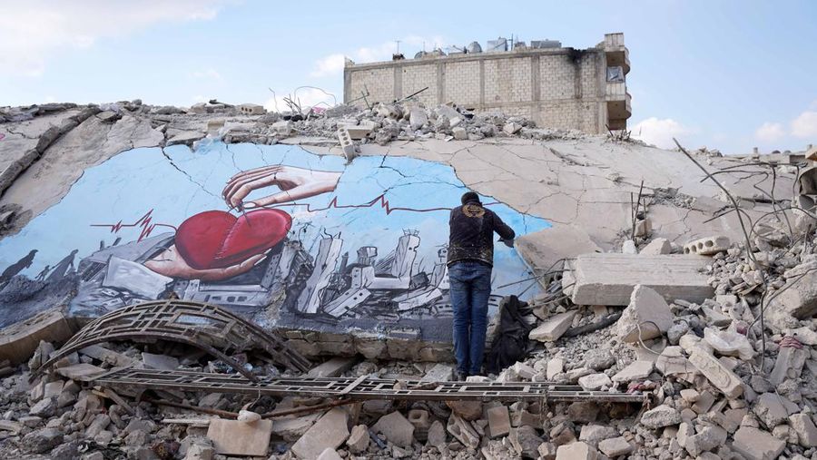 Seniman grafiti Suriah Aziz Asmar, Salam Hamid dan Muhammad Enis Hamdun melukis perjuangan gempa bumi di atas puing-puing bangunan yang runtuh di Jindires, sebuah distrik di Afrin yang terkena dampak gempa bumi Turkiye-Suriah 06 Februari di Aleppo, Suriah pada 22 Februari, 2023. (Omer Alven/Anadolu Agency via Getty Images)