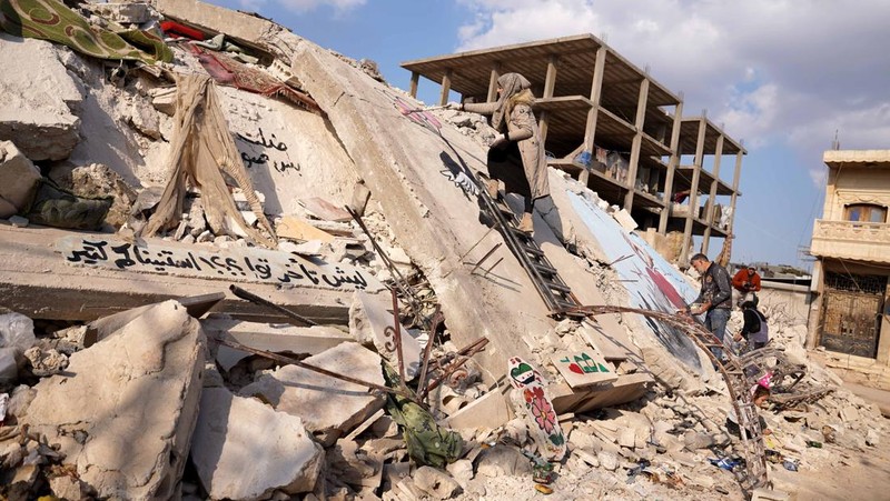 Seniman grafiti Suriah Aziz Asmar, Salam Hamid dan Muhammad Enis Hamdun melukis perjuangan gempa bumi di atas puing-puing bangunan yang runtuh di Jindires, sebuah distrik di Afrin yang terkena dampak gempa bumi Turkiye-Suriah 06 Februari di Aleppo, Suriah pada 22 Februari, 2023. (Omer Alven/Anadolu Agency via Getty Images)