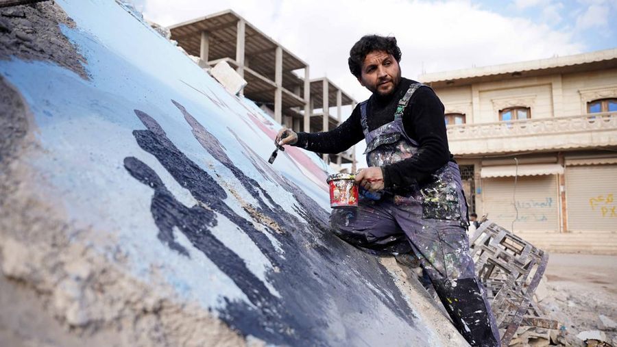Seniman grafiti Suriah Aziz Asmar, Salam Hamid dan Muhammad Enis Hamdun melukis perjuangan gempa bumi di atas puing-puing bangunan yang runtuh di Jindires, sebuah distrik di Afrin yang terkena dampak gempa bumi Turkiye-Suriah 06 Februari di Aleppo, Suriah pada 22 Februari, 2023. (Omer Alven/Anadolu Agency via Getty Images)