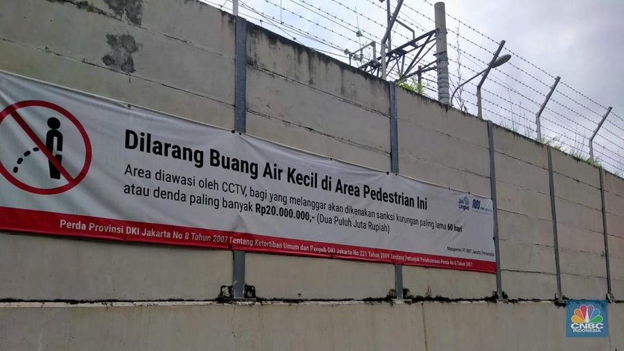 Warga melewati spanduk larangan encing di pinggir Jakarta, 'Kena' Rp 20 Juta di kawasan Lebak Bulus, Jakarta, Kamis (23/2/2023). (CNBC Indonesia/Suhendra)