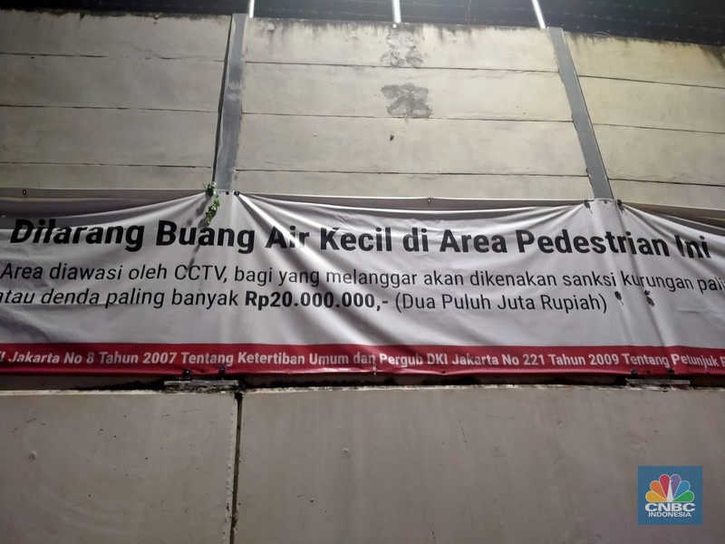 Warga melewati spanduk larangan encing di pinggir Jakarta, 'Kena' Rp 20 Juta di kawasan Lebak Bulus, Jakarta, Kamis (23/2/2023). (CNBC Indonesia/Suhendra)