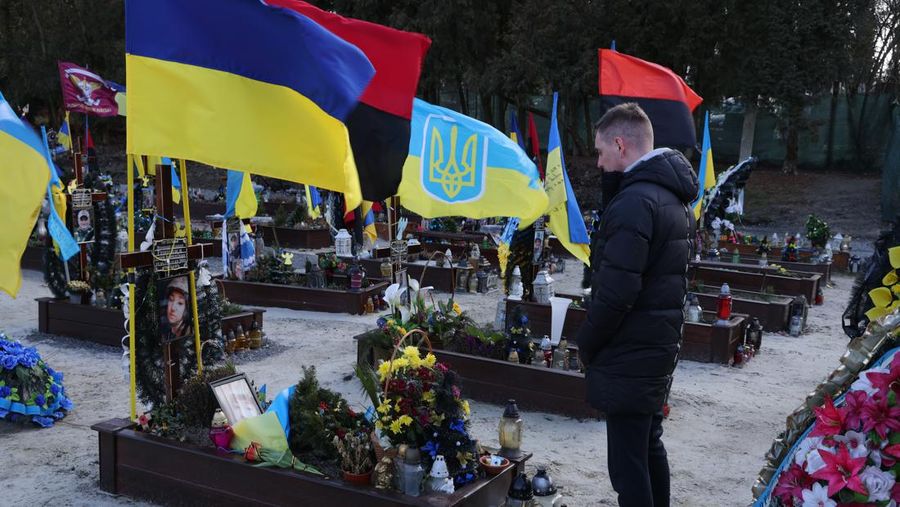 Denys, yang memilih untuk tidak mengungkapkan nama belakangnya, berdiri diam di makam Ksenia Gritsina, 29, yang adalah seorang sersan dan petugas medis di angkatan bersenjata Ukraina, di antara bendera yang berkibar di atas kuburan tentara lain di pemakaman Field of Mars di 23 Februari 2023 di Lviv, Ukraina. Denys adalah komandan unit Ksenia. 
