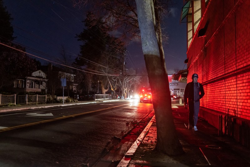 Seorang pria berjalan di sepanjang jalan kosong dalam kegelapan, menyusul badai musim dingin yang besar yang meninggalkan rumah dan bisnis tanpa listrik, di Menlo Park, California A.S., 21 Februari 2023. (REUTERS/ Carlos Barria)