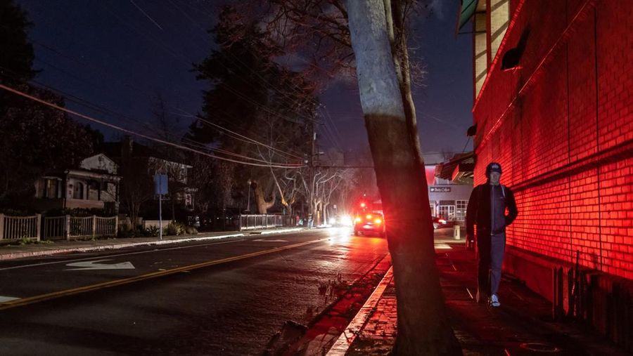 Seorang pria berjalan di sepanjang jalan kosong dalam kegelapan, menyusul badai musim dingin yang besar yang meninggalkan rumah dan bisnis tanpa listrik, di Menlo Park, California A.S., 21 Februari 2023. (REUTERS/ Carlos Barria)