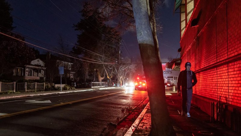 Seorang pria berjalan di sepanjang jalan kosong dalam kegelapan, menyusul badai musim dingin yang besar yang meninggalkan rumah dan bisnis tanpa listrik, di Menlo Park, California A.S., 21 Februari 2023. (REUTERS/ Carlos Barria)