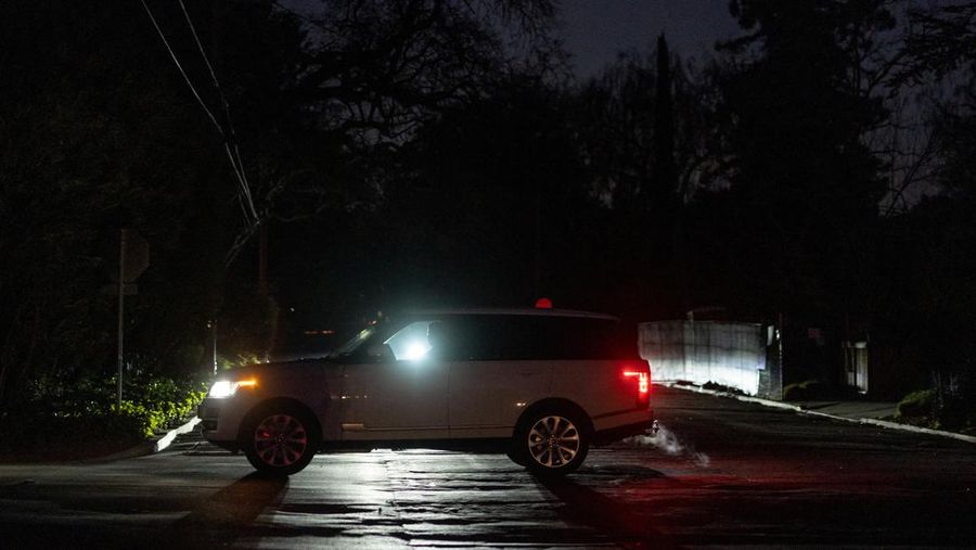 Seorang pria berjalan di sepanjang jalan kosong dalam kegelapan, menyusul badai musim dingin yang besar yang meninggalkan rumah dan bisnis tanpa listrik, di Menlo Park, California A.S., 21 Februari 2023. (REUTERS/ Carlos Barria)