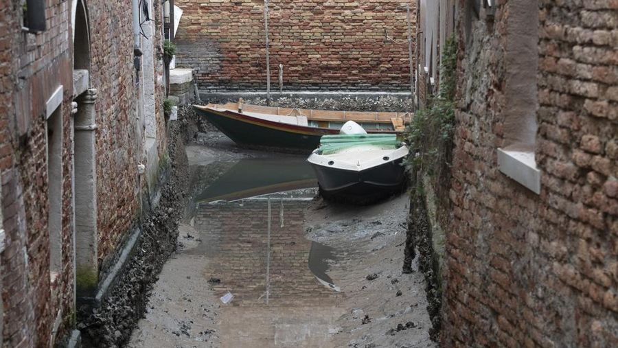 Boats are docked along a dried canal during a low tide in Venice, Italy, Tuesday, Feb. 21, 2023. Some of Venice's secondary canals have practically dried up lately due a prolonged spell of low tides linked to a lingering high-pressure weather system. (AP Photo/Luigi Costantini)