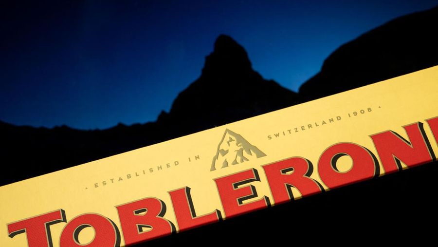 Sebuah gambar yang diambil pada 6 Maret 2023 di Jenewa memperlihatkan kemasan cokelat batangan Toblerone milik perusahaan AS Mondelez dengan gambar gunung Matterhorn yang terlihat dalam siluet di latar belakang. - Toblerone akan menghapus puncak Matterhorn Swiss yang ikonik dari kemasannya ketika beberapa produksi cokelat dipindahkan dari Swiss ke Slovakia dan digantikan oleh gunung yang lebih umum di bawah aturan 
