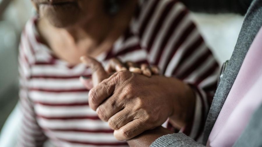 Nurse or home caregiver and senior woman holding hands at home