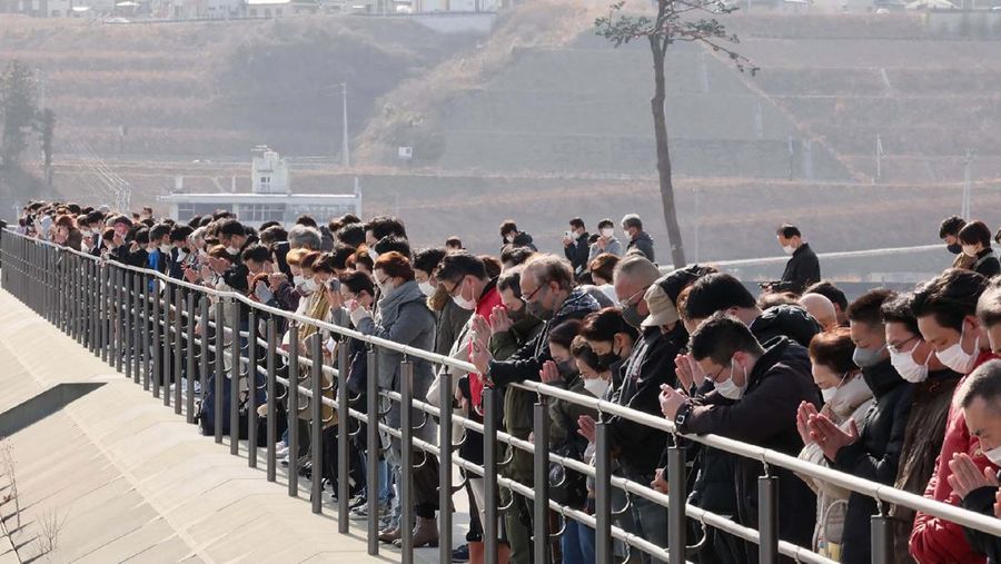 Orang-orang berkumpul di Natori, Prefektur Miyagi, Jepang untuk mengenang para korban pada peringatan 12 tahun gempa bumi, tsunami, dan bencana nuklir 2011. (STR/JIJI PRESS/AFP via Getty Images)