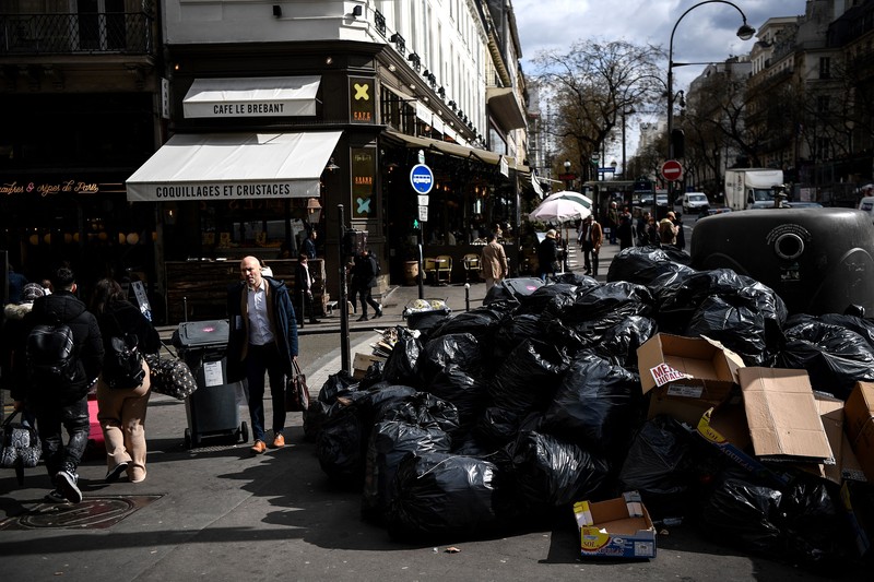 A worker walks past a pile of garbage bags that have been piling up since waste collectors went on strike against the French government's proposed pensions reform, in front of the Eiffel tower in Paris on March 15, 2023. - France faces another day of strikes on march 15, 2023, over highly contested pension reforms which President appears on the verge of pushing through despite months of protests. As the legislation enters the final stretch in parliament, trade unions are set to make another attempt to pressure the government and lawmakers into rejecting the proposed hike in the retirement age to 64. (Photo by Christophe ARCHAMBAULT / AFP) (Photo by CHRISTOPHE ARCHAMBAULT/AFP via Getty Images)