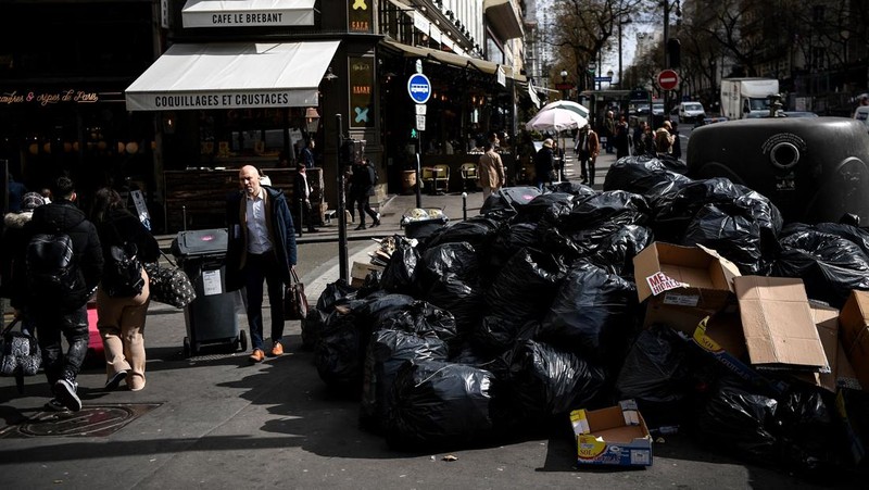 A worker walks past a pile of garbage bags that have been piling up since waste collectors went on strike against the French government's proposed pensions reform, in front of the Eiffel tower in Paris on March 15, 2023. - France faces another day of strikes on march 15, 2023, over highly contested pension reforms which President appears on the verge of pushing through despite months of protests. As the legislation enters the final stretch in parliament, trade unions are set to make another attempt to pressure the government and lawmakers into rejecting the proposed hike in the retirement age to 64. (Photo by Christophe ARCHAMBAULT / AFP) (Photo by CHRISTOPHE ARCHAMBAULT/AFP via Getty Images)