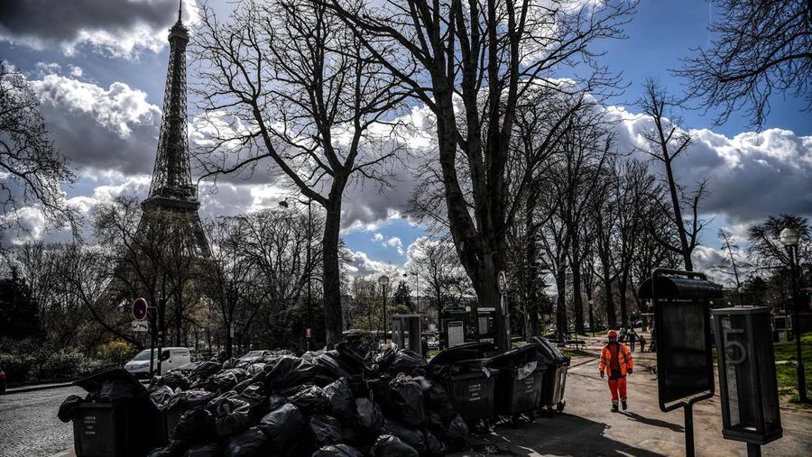 A worker walks past a pile of garbage bags that have been piling up since waste collectors went on strike against the French government's proposed pensions reform, in front of the Eiffel tower in Paris on March 15, 2023. - France faces another day of strikes on march 15, 2023, over highly contested pension reforms which President appears on the verge of pushing through despite months of protests. As the legislation enters the final stretch in parliament, trade unions are set to make another attempt to pressure the government and lawmakers into rejecting the proposed hike in the retirement age to 64. (Photo by Christophe ARCHAMBAULT / AFP) (Photo by CHRISTOPHE ARCHAMBAULT/AFP via Getty Images)