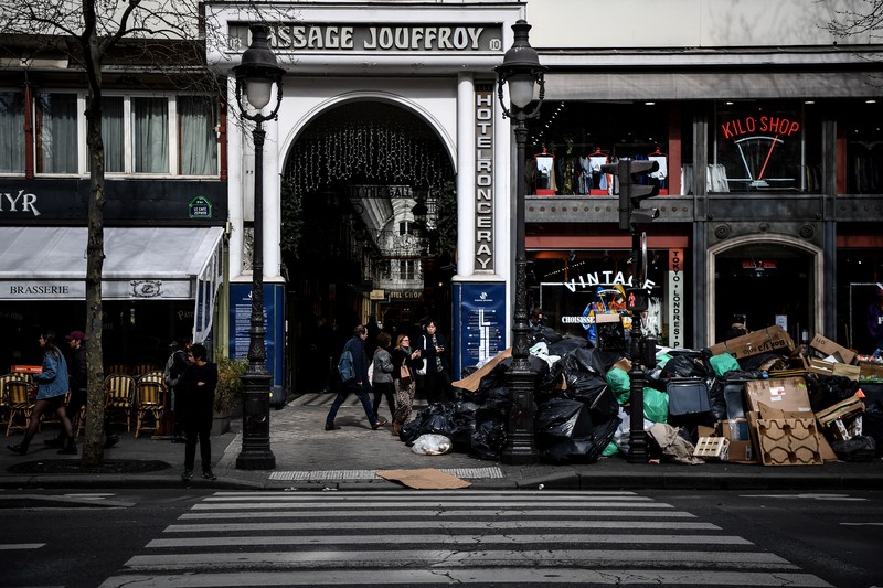 A worker walks past a pile of garbage bags that have been piling up since waste collectors went on strike against the French government's proposed pensions reform, in front of the Eiffel tower in Paris on March 15, 2023. - France faces another day of strikes on march 15, 2023, over highly contested pension reforms which President appears on the verge of pushing through despite months of protests. As the legislation enters the final stretch in parliament, trade unions are set to make another attempt to pressure the government and lawmakers into rejecting the proposed hike in the retirement age to 64. (Photo by Christophe ARCHAMBAULT / AFP) (Photo by CHRISTOPHE ARCHAMBAULT/AFP via Getty Images)