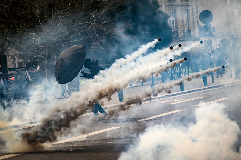 1248321815 TOPSHOT - A protestor holds an umbrella to protect from teargas during a demonstration on the 8th day of strikes and protests across the country against the government's proposed pensions overhaul, in Nantes, on March 15, 2023. - France faces another day of strikes over highly contested pension reforms which President appears on the verge of pushing through despite months of protests. As the legislation enters the final stretch in parliament, trade unions are set to make another attempt to pressure the government and lawmakers into rejecting the proposed hike in the retirement age to 64. (Photo by LOIC VENANCE / AFP) (Photo by LOIC VENANCE/AFP via Getty Images)