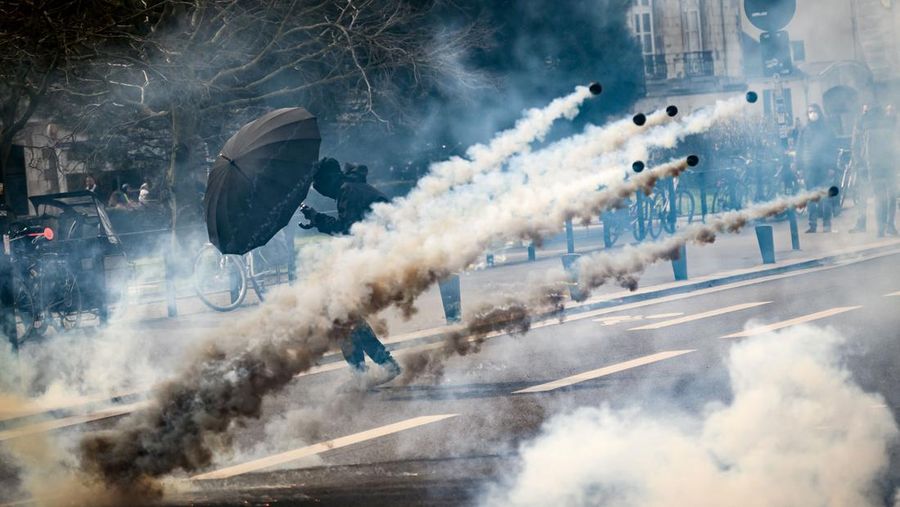 TOPSHOT - A protestor holds an umbrella to protect from teargas during a demonstration on the 8th day of strikes and protests across the country against the government's proposed pensions overhaul, in Nantes, on March 15, 2023. - France faces another day of strikes over highly contested pension reforms which President appears on the verge of pushing through despite months of protests. As the legislation enters the final stretch in parliament, trade unions are set to make another attempt to pressure the government and lawmakers into rejecting the proposed hike in the retirement age to 64. (Photo by LOIC VENANCE / AFP) (Photo by LOIC VENANCE/AFP via Getty Images)