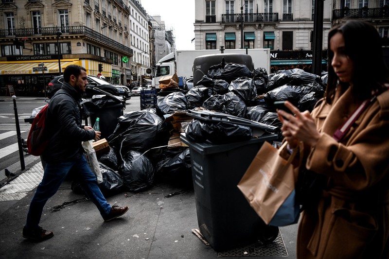 A worker walks past a pile of garbage bags that have been piling up since waste collectors went on strike against the French government's proposed pensions reform, in front of the Eiffel tower in Paris on March 15, 2023. - France faces another day of strikes on march 15, 2023, over highly contested pension reforms which President appears on the verge of pushing through despite months of protests. As the legislation enters the final stretch in parliament, trade unions are set to make another attempt to pressure the government and lawmakers into rejecting the proposed hike in the retirement age to 64. (Photo by Christophe ARCHAMBAULT / AFP) (Photo by CHRISTOPHE ARCHAMBAULT/AFP via Getty Images)