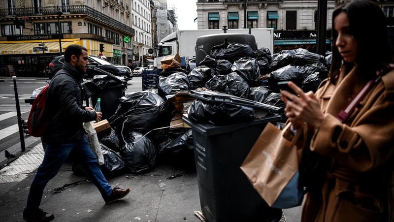 A worker walks past a pile of garbage bags that have been piling up since waste collectors went on strike against the French government's proposed pensions reform, in front of the Eiffel tower in Paris on March 15, 2023. - France faces another day of strikes on march 15, 2023, over highly contested pension reforms which President appears on the verge of pushing through despite months of protests. As the legislation enters the final stretch in parliament, trade unions are set to make another attempt to pressure the government and lawmakers into rejecting the proposed hike in the retirement age to 64. (Photo by Christophe ARCHAMBAULT / AFP) (Photo by CHRISTOPHE ARCHAMBAULT/AFP via Getty Images)