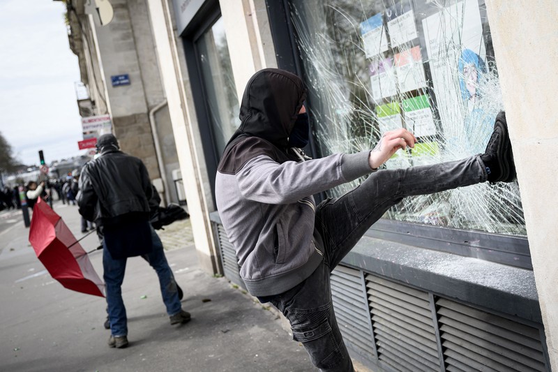 TOPSHOT - A protestor holds an umbrella to protect from teargas during a demonstration on the 8th day of strikes and protests across the country against the government's proposed pensions overhaul, in Nantes, on March 15, 2023. - France faces another day of strikes over highly contested pension reforms which President appears on the verge of pushing through despite months of protests. As the legislation enters the final stretch in parliament, trade unions are set to make another attempt to pressure the government and lawmakers into rejecting the proposed hike in the retirement age to 64. (Photo by LOIC VENANCE / AFP) (Photo by LOIC VENANCE/AFP via Getty Images)