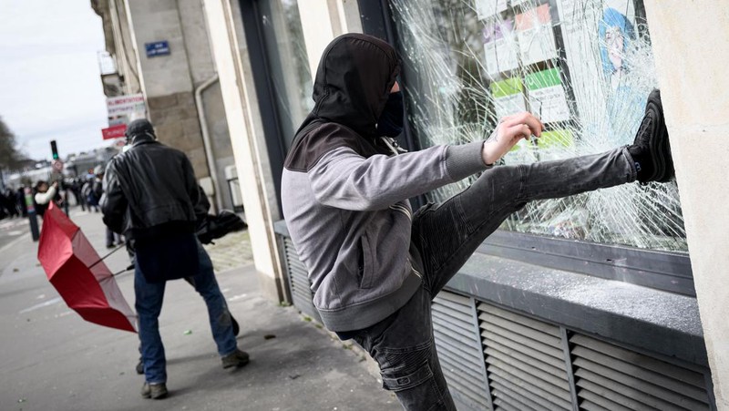 TOPSHOT - A protestor holds an umbrella to protect from teargas during a demonstration on the 8th day of strikes and protests across the country against the government's proposed pensions overhaul, in Nantes, on March 15, 2023. - France faces another day of strikes over highly contested pension reforms which President appears on the verge of pushing through despite months of protests. As the legislation enters the final stretch in parliament, trade unions are set to make another attempt to pressure the government and lawmakers into rejecting the proposed hike in the retirement age to 64. (Photo by LOIC VENANCE / AFP) (Photo by LOIC VENANCE/AFP via Getty Images)