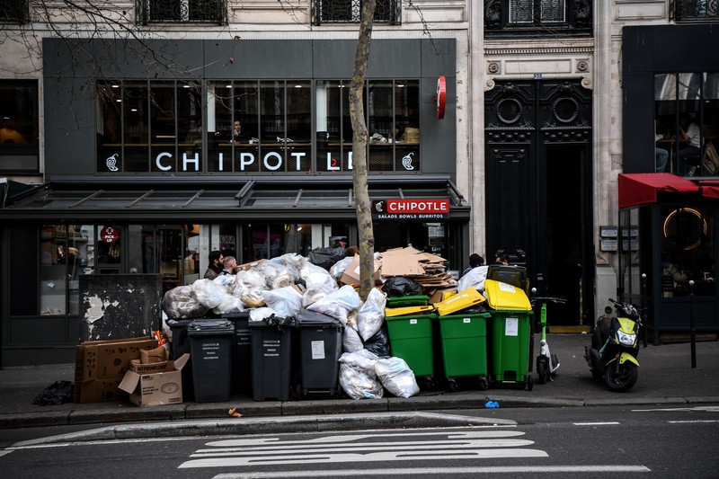 A worker walks past a pile of garbage bags that have been piling up since waste collectors went on strike against the French government's proposed pensions reform, in front of the Eiffel tower in Paris on March 15, 2023. - France faces another day of strikes on march 15, 2023, over highly contested pension reforms which President appears on the verge of pushing through despite months of protests. As the legislation enters the final stretch in parliament, trade unions are set to make another attempt to pressure the government and lawmakers into rejecting the proposed hike in the retirement age to 64. (Photo by Christophe ARCHAMBAULT / AFP) (Photo by CHRISTOPHE ARCHAMBAULT/AFP via Getty Images)